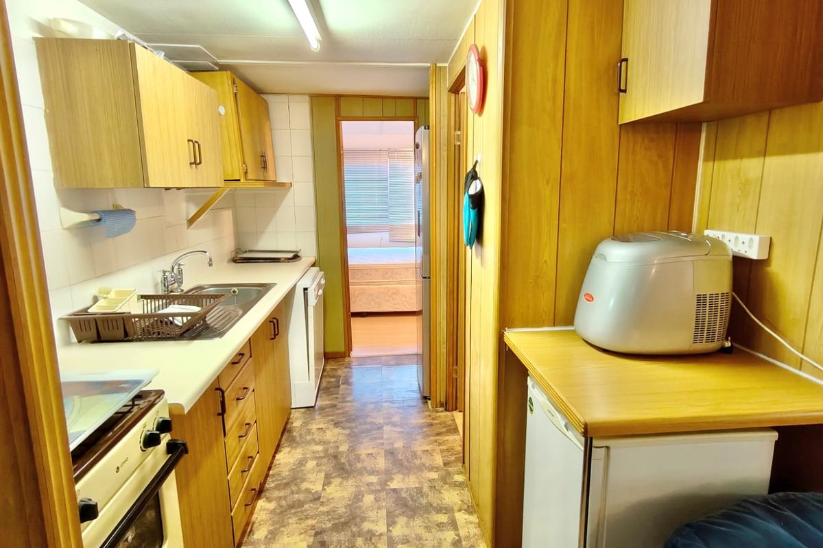 A compact, dated kitchen featuring laminate cabinetry, tiled splashbacks, and a freestanding oven, with direct access to an adjacent bedroom.