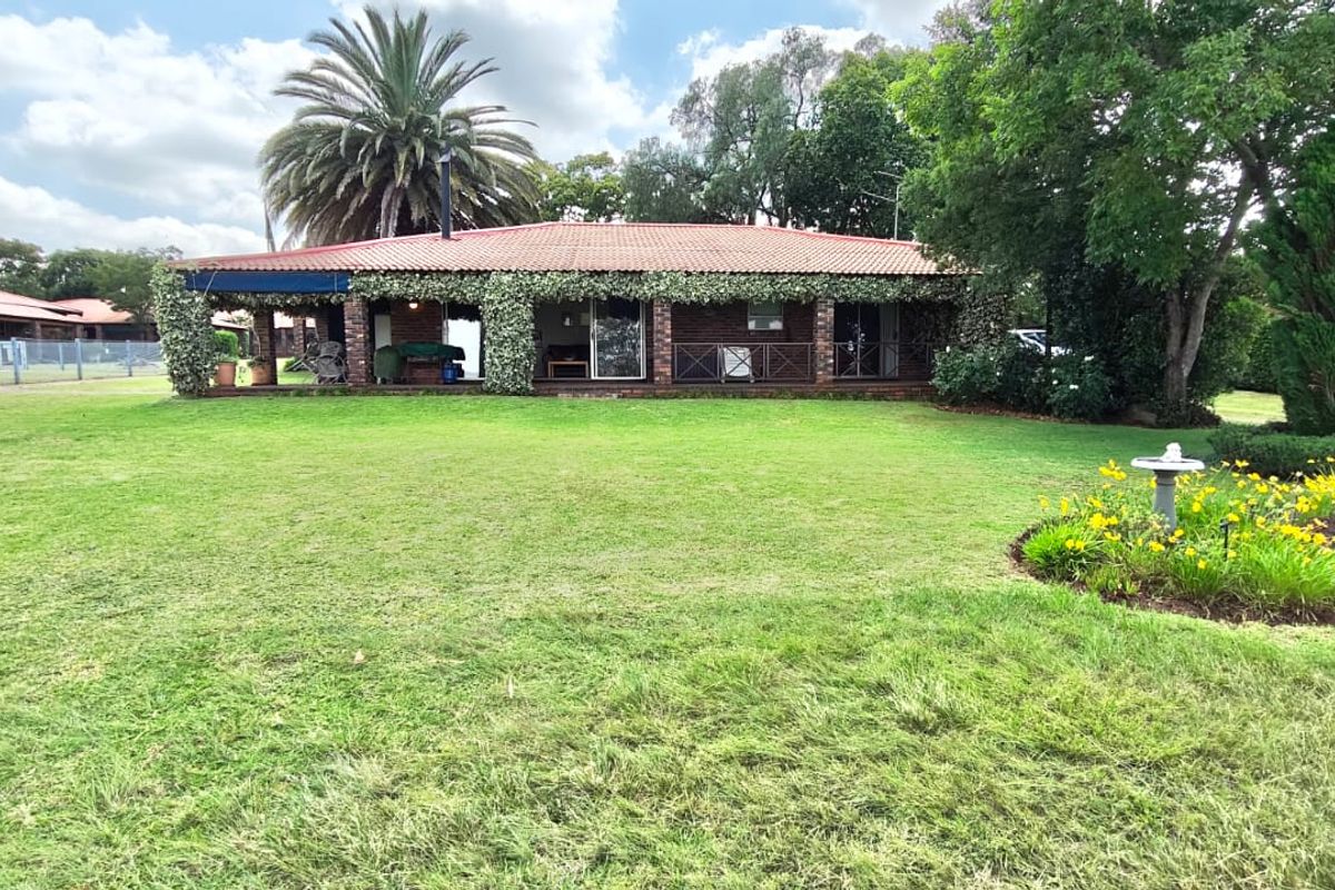 A rear view of a brick house featuring a covered patio area overlooking a spacious, well-maintained lawn and garden.