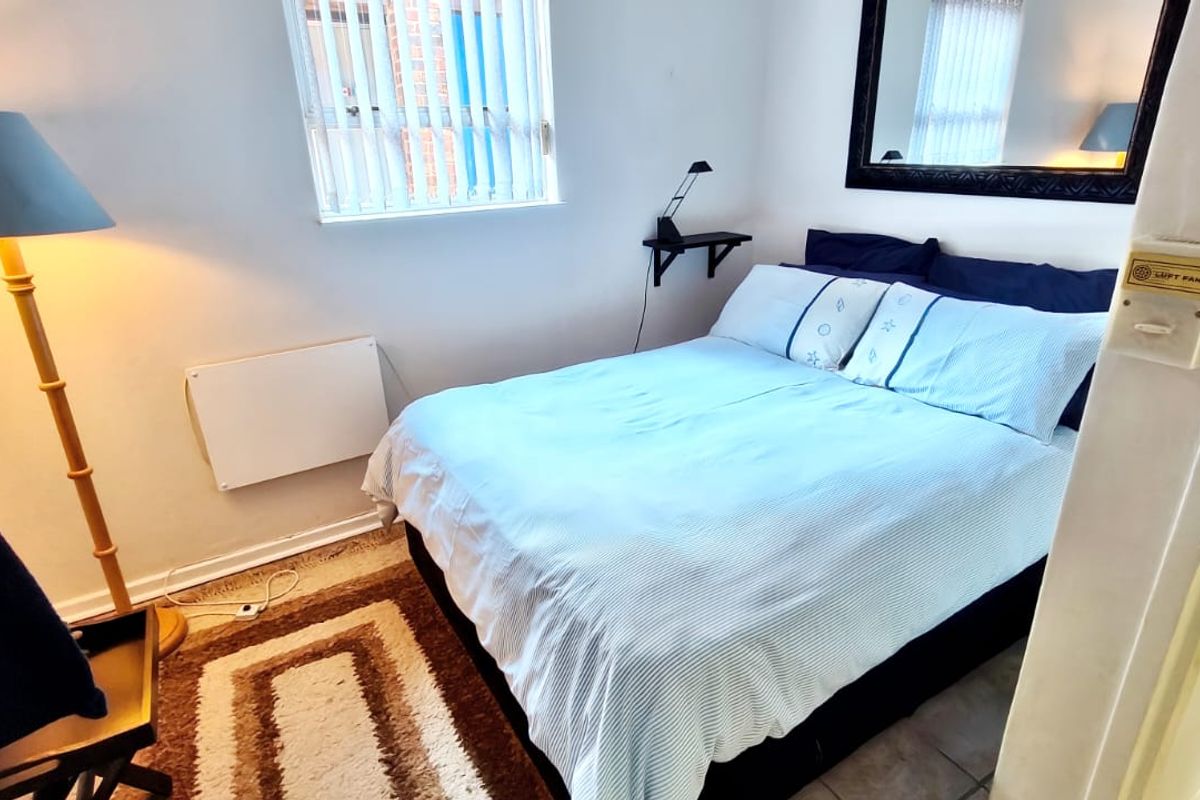 A compact bedroom featuring a wall-mounted electric heater, vertical window blinds, and neutral wall finishes.
