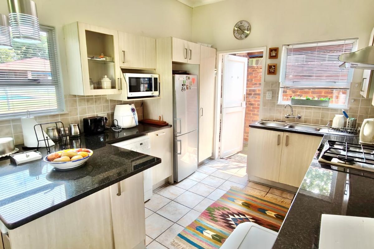 A functional kitchen featuring granite countertops, light wood-finish cabinetry, a gas hob with extractor fan, and direct access to an exterior area.