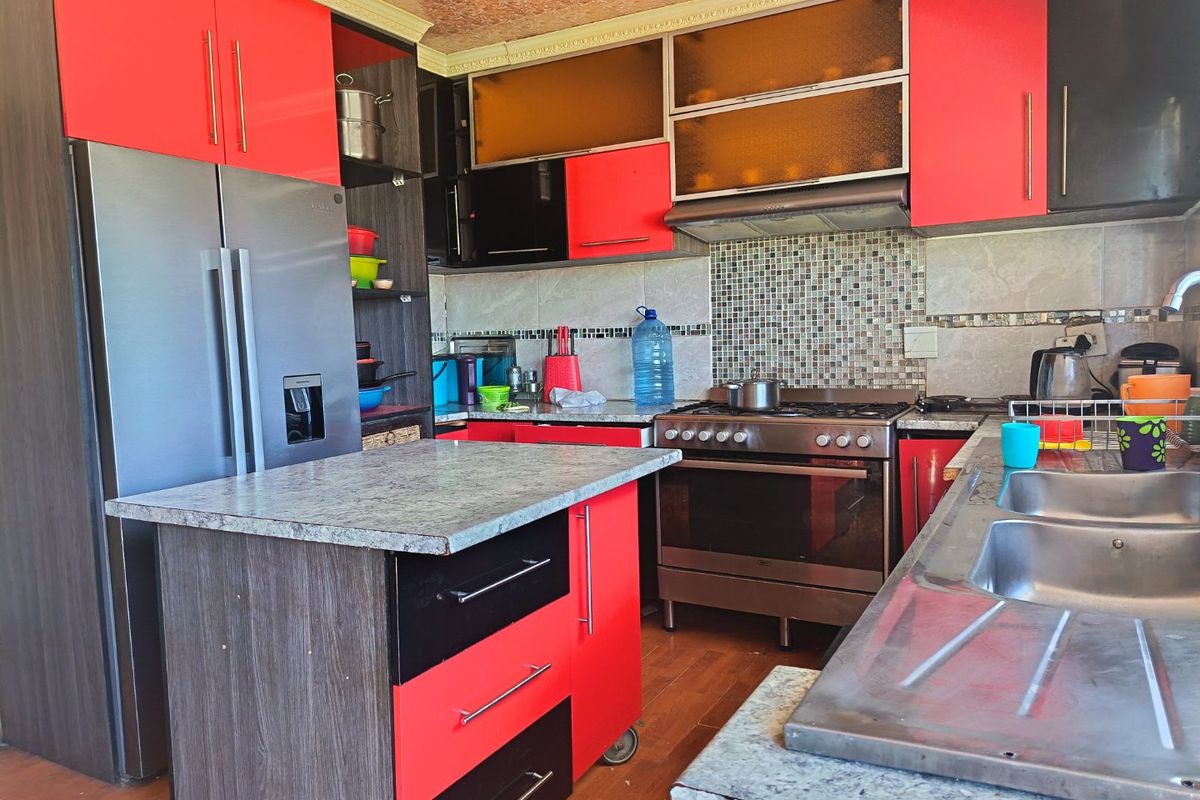 A functional kitchen featuring red and black cabinetry, a central island, stainless steel stove with extractor fan, and a double sink with tiled backsplash.