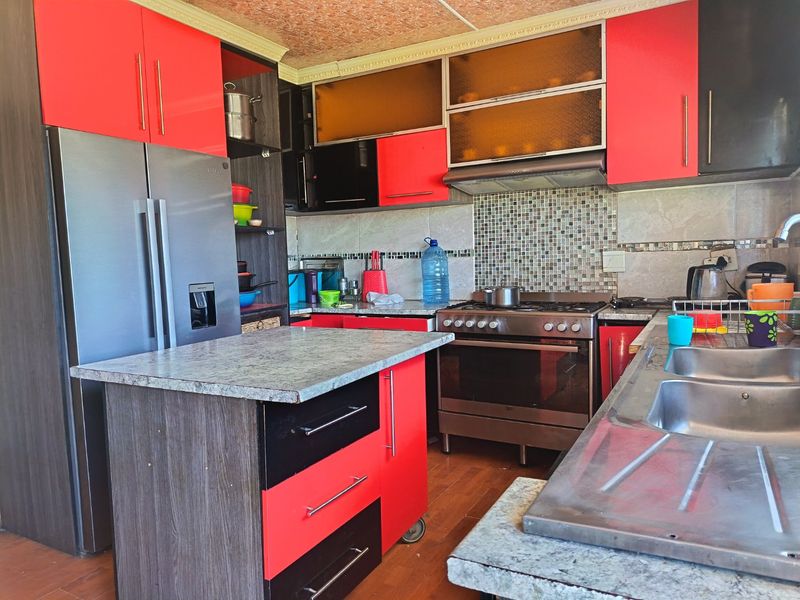 A functional kitchen featuring red and black cabinetry, a central island, stainless steel stove with extractor fan, and a double sink with tiled backsplash.