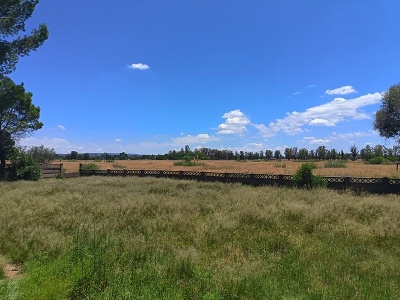 Expansive view of the open farm landscape, featuring a precast concrete boundary wall and natural grass fields under a clear blue sky.