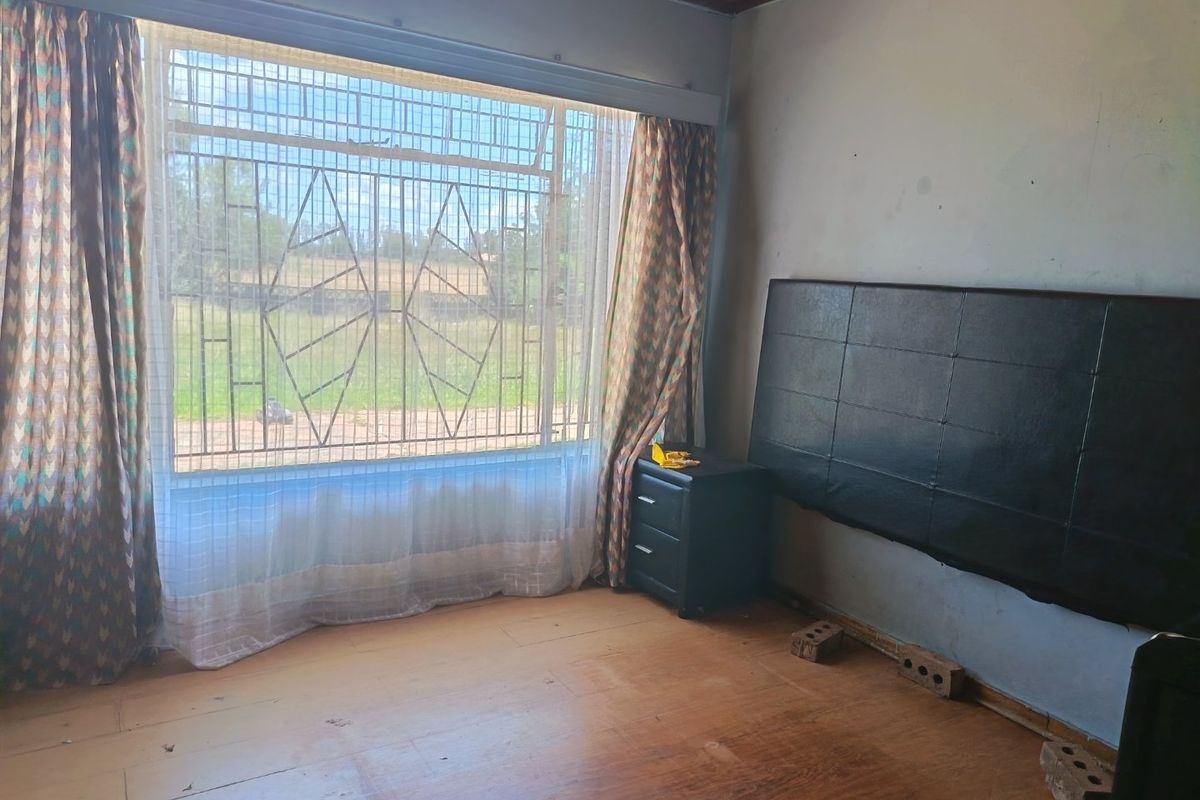 A bedroom featuring timber ceilings, laminate flooring, and large windows with security bars, offering a blank canvas for renovation and modernization.