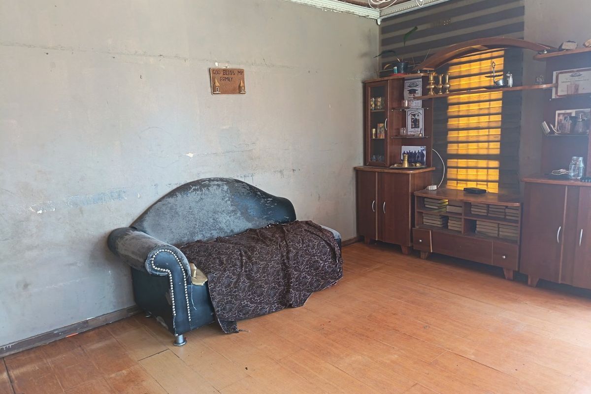 A living room featuring wooden flooring, ceiling cornice, and a chandelier, requiring cosmetic updates to the wall finishes and general maintenance.