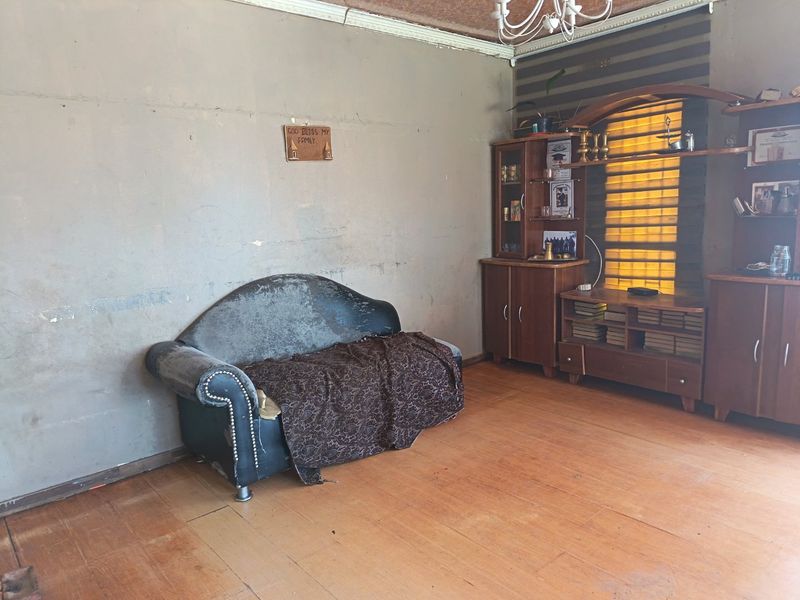 A living room featuring wooden flooring, ceiling cornice, and a chandelier, requiring cosmetic updates to the wall finishes and general maintenance.