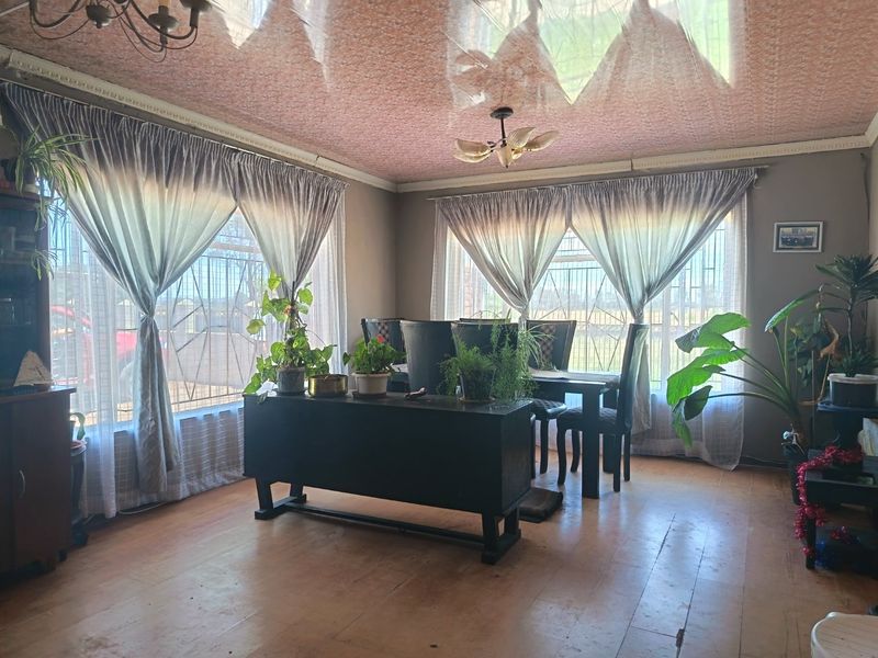 A dining room featuring hardwood flooring, decorative ceiling finishes, and large windows with security bars, offering a functional space with potential for modernization.