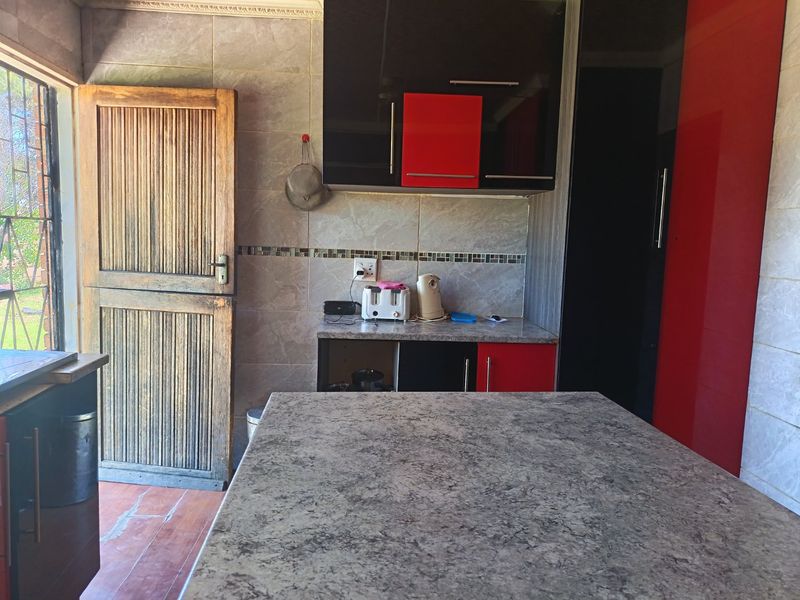 Kitchen area featuring high-gloss red and black cabinetry, stone-look countertops, and tiled walls, with direct access to an outdoor area via a timber door.