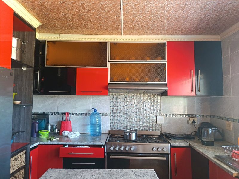 A functional kitchen featuring red and black cabinetry, a gas hob with extractor fan, and a mosaic tile backsplash.