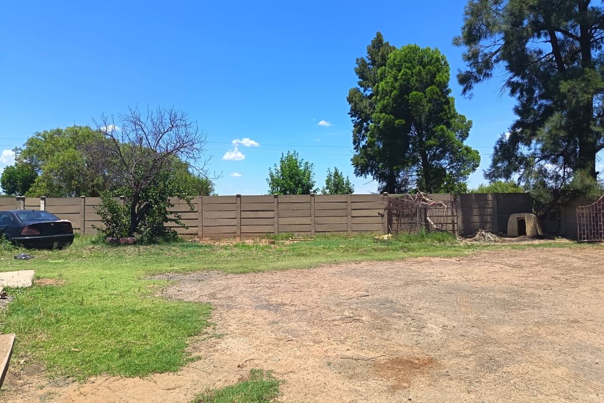 A spacious rear yard area featuring a precast concrete boundary wall and established trees on a large farm property.