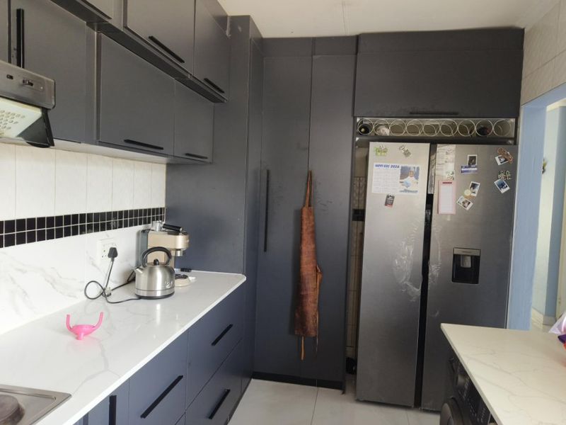Modern kitchen featuring dark grey cabinetry, stone countertops, a tiled backsplash, and integrated storage solutions.