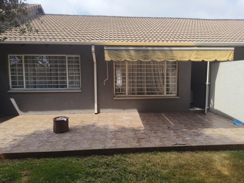Rear exterior view of the apartment featuring a tiled patio area, retractable awning, and security bars on the windows.