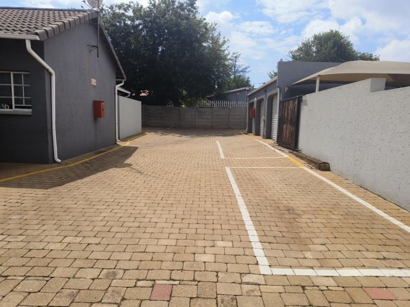 A paved exterior area featuring marked parking bays, boundary walls, and access to garage units.