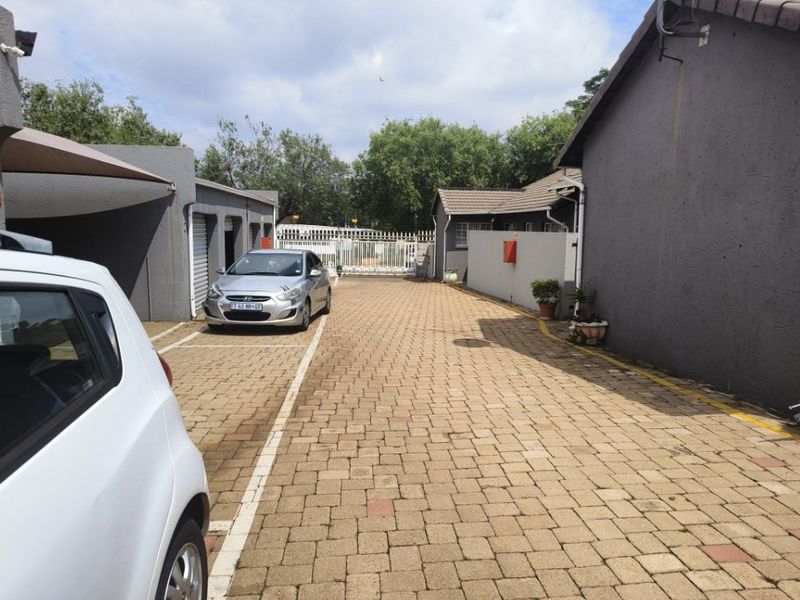 A paved driveway leading to a secure gated entrance with covered parking and exterior building facades.