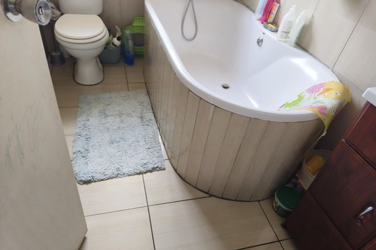A functional bathroom featuring a bathtub with tiled surround, a standard toilet, and neutral floor tiling.