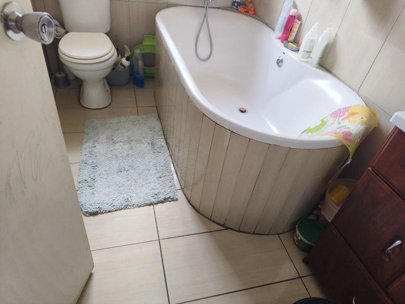 A functional bathroom featuring a bathtub with tiled surround, a standard toilet, and neutral floor tiling.