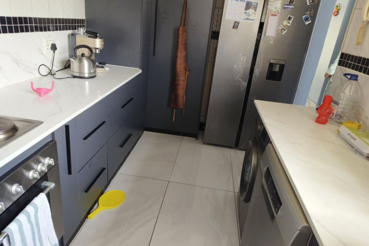 Modern kitchen featuring dark cabinetry, white quartz countertops, tiled flooring, and integrated appliances, offering a clean and functional workspace.
