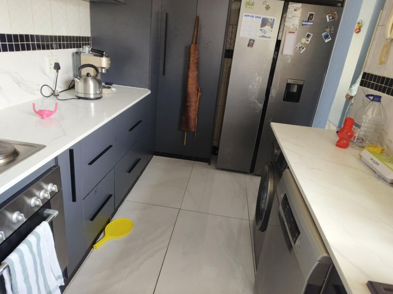 Modern kitchen featuring dark cabinetry, white quartz countertops, tiled flooring, and integrated appliances, offering a clean and functional workspace.