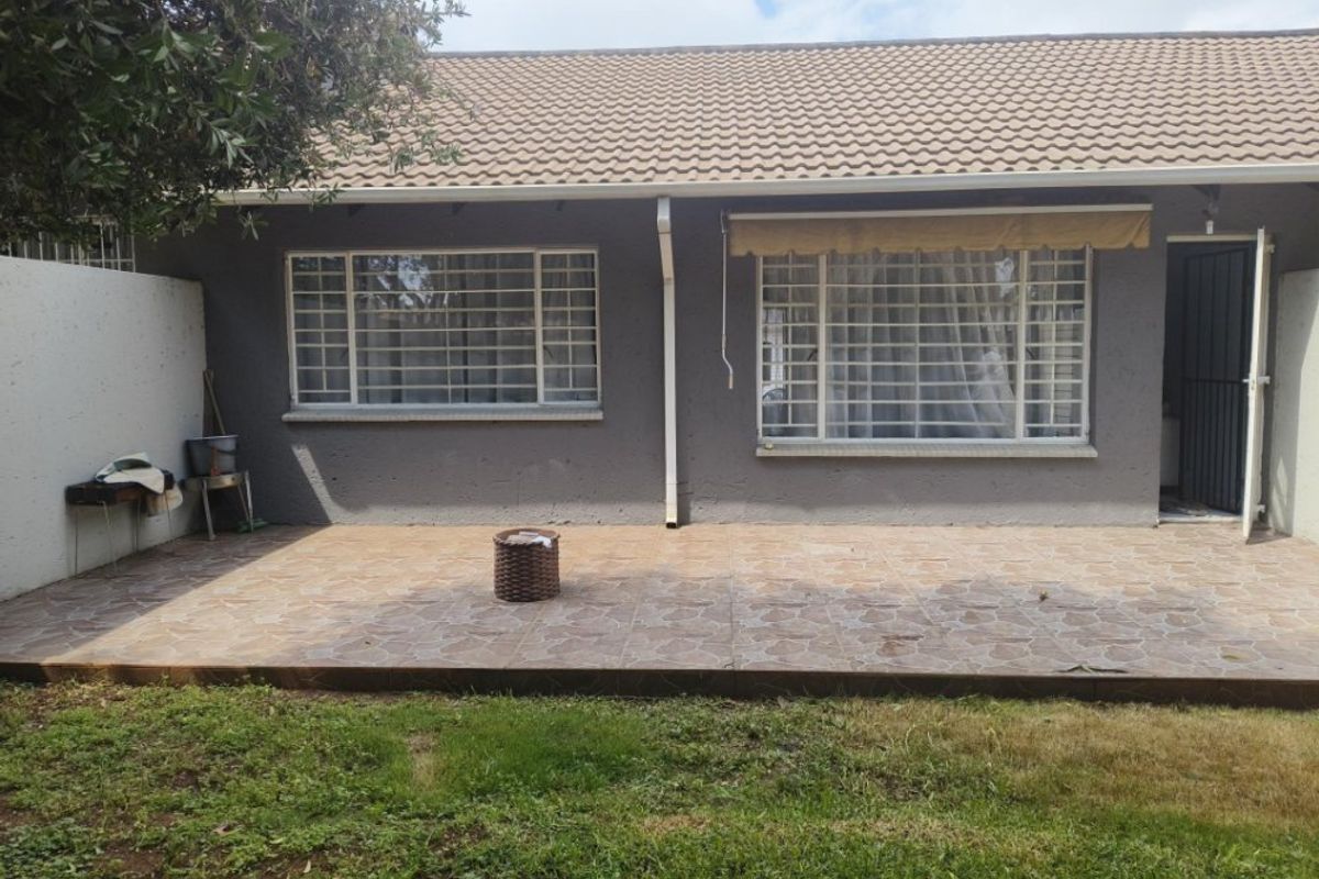 Rear exterior view of the apartment featuring a tiled patio area, security bars on windows, and a covered entrance.