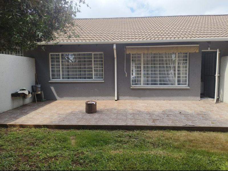 Rear exterior view of the apartment featuring a tiled patio area, security bars on windows, and a covered entrance.
