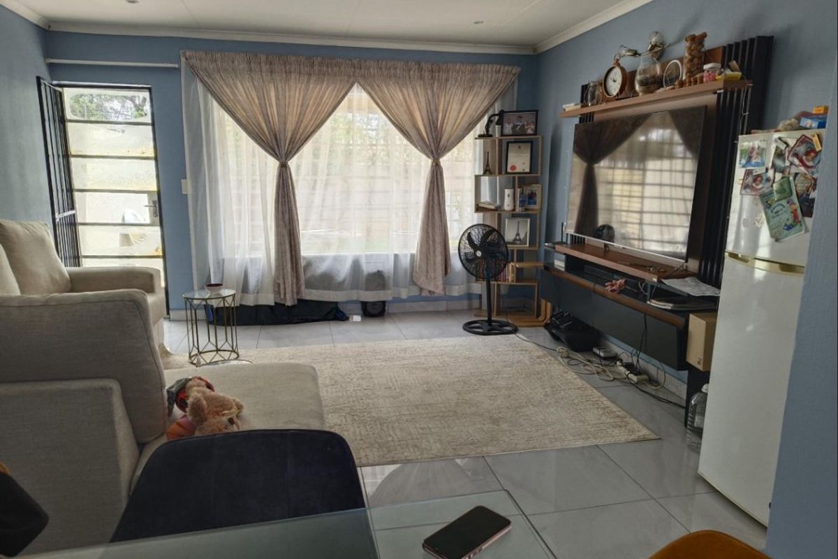 A comfortable living room featuring tiled flooring, recessed lighting, and a built-in media console, with direct access to an outdoor area via a security gate.