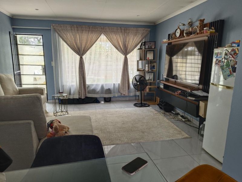 A comfortable living room featuring tiled flooring, recessed lighting, and a built-in media console, with direct access to an outdoor area via a security gate.