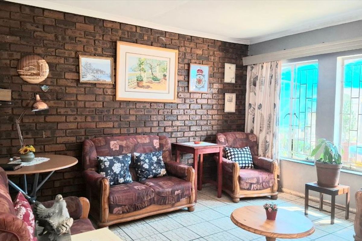 A living room featuring an exposed brick feature wall, tiled flooring, and large windows fitted with security bars.
