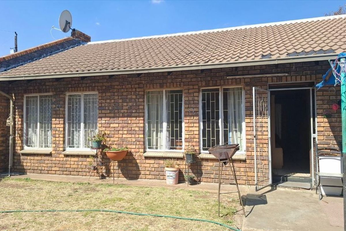 Rear view of a face brick house featuring a tiled roof, security bars on windows, and a concrete patio area.