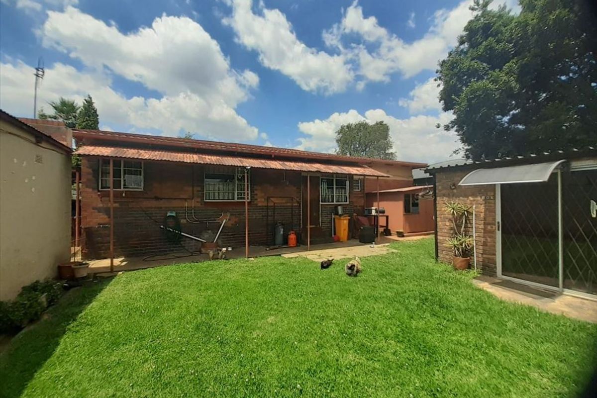 Rear view of the property featuring a brick facade, corrugated metal roof, and a private garden area with a concrete patio.