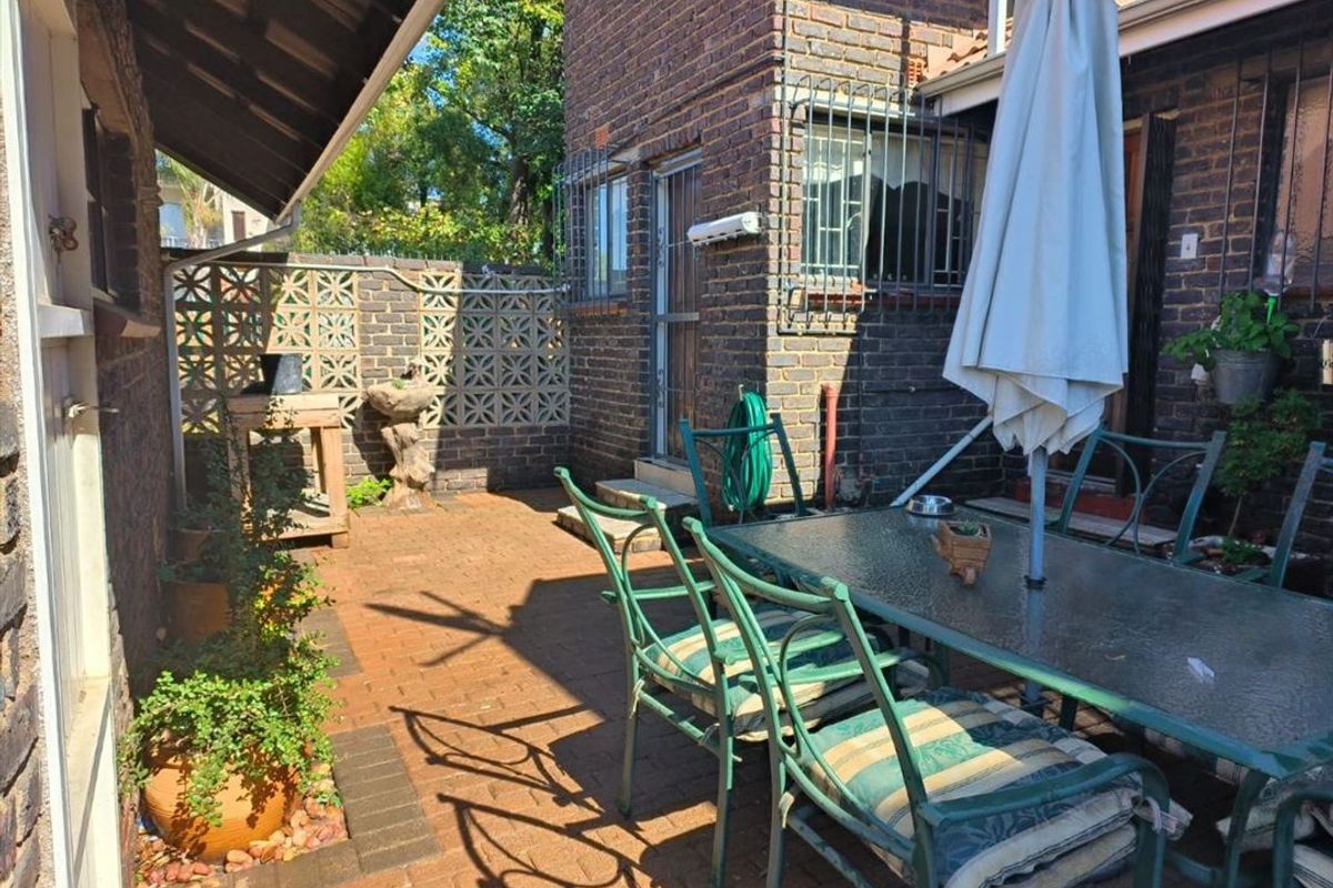 A paved outdoor patio area featuring brick walls with decorative breeze blocks and security-fitted windows, providing a functional space for outdoor dining.