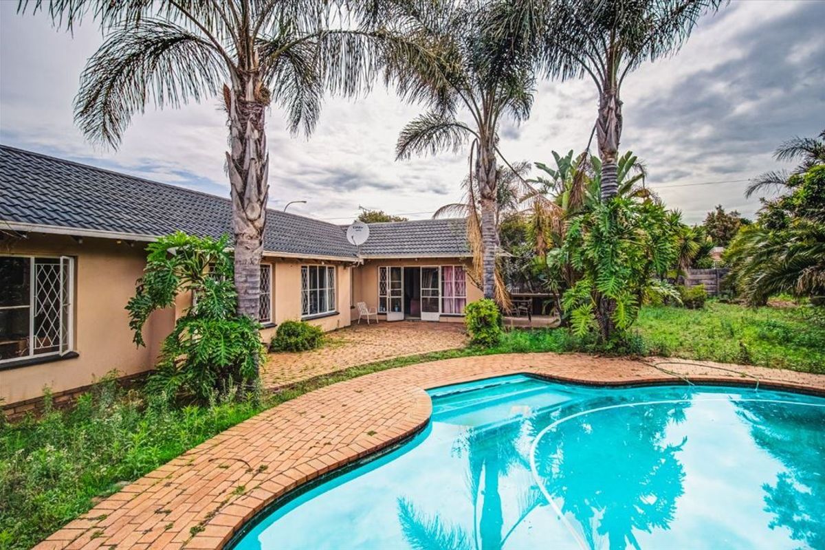 Rear exterior view featuring a swimming pool, brick paved patio area, and established palm trees set against the back facade of the house.