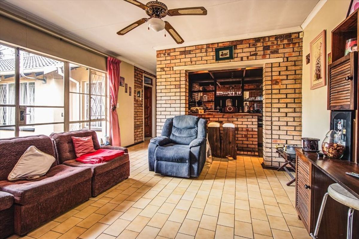 A living room featuring exposed brick walls, tiled flooring, a ceiling fan, and an integrated bar area with brick counter.