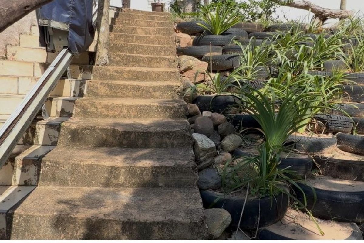 Outdoor concrete staircase featuring an installed stair lift and a retaining wall constructed from recycled tires.