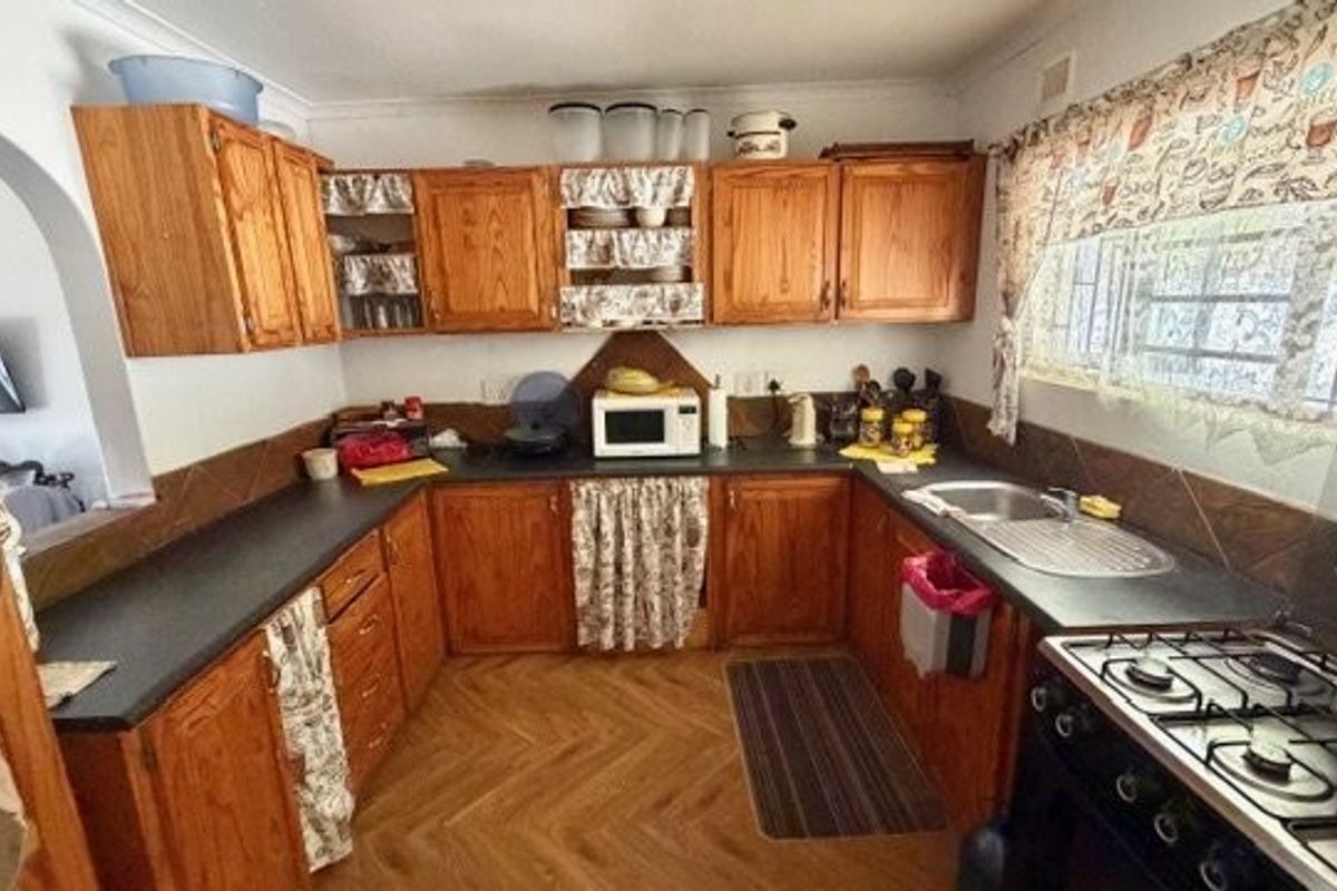 A functional kitchen featuring traditional wooden cabinetry, dark laminate countertops, a gas hob, and parquet flooring, offering potential for a modern update.