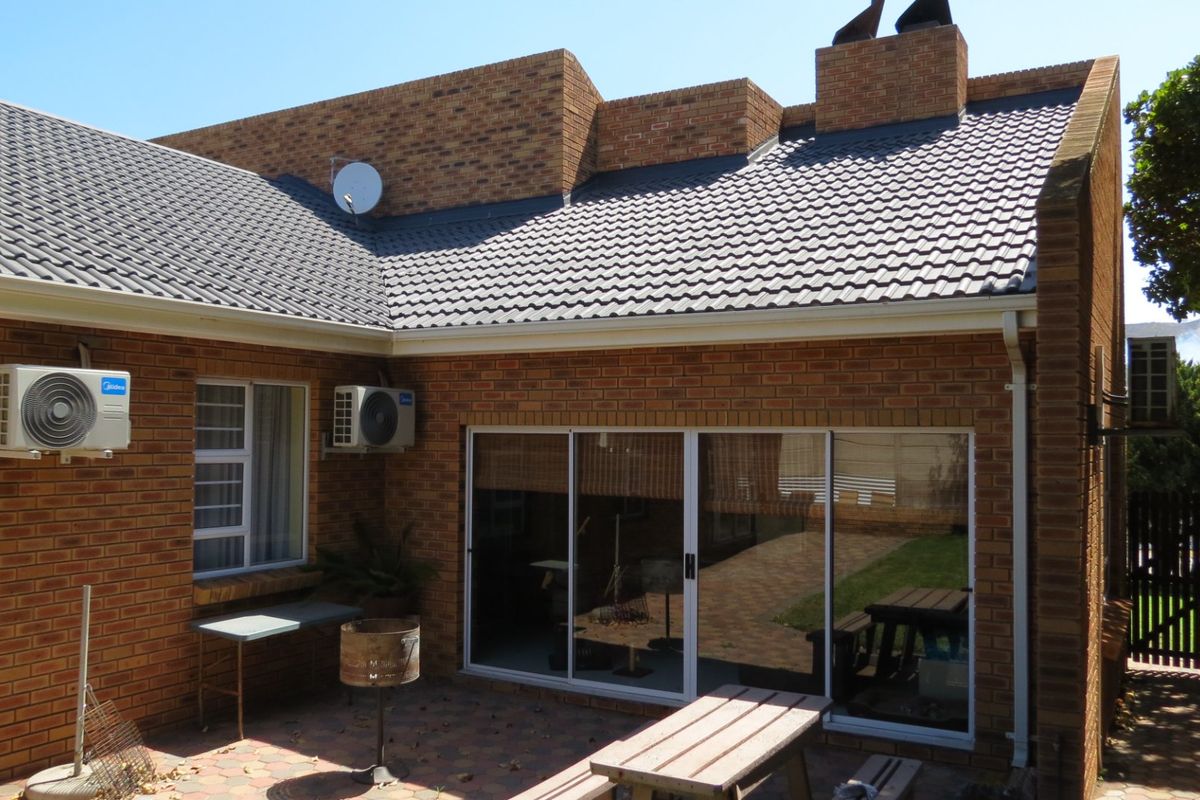 Rear view of the house featuring a face brick facade, tiled roof, paved patio area, and sliding glass doors providing access to the interior.