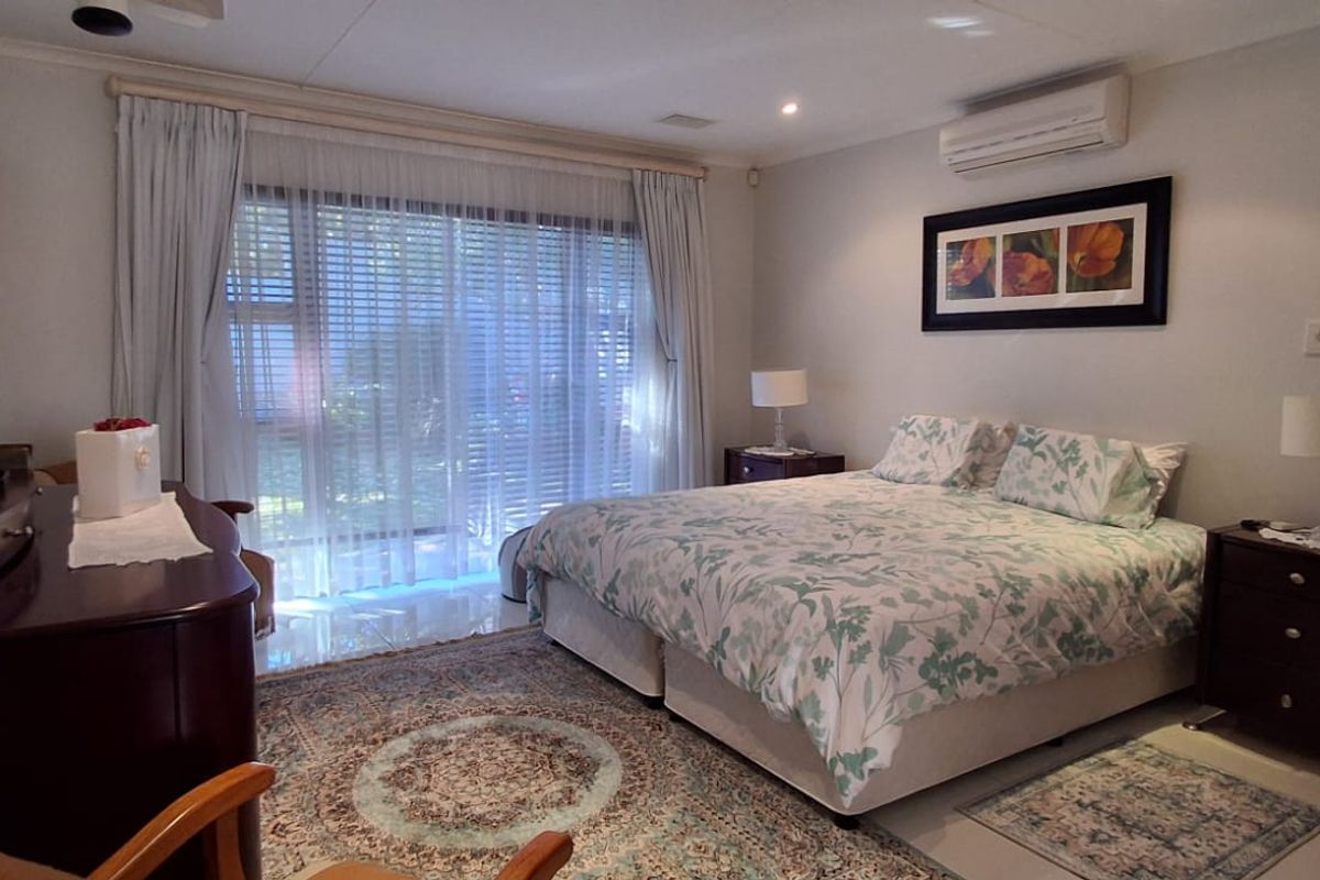 A well-maintained bedroom featuring tiled flooring, a split-system air conditioner, and large sliding glass doors providing natural light and garden access.