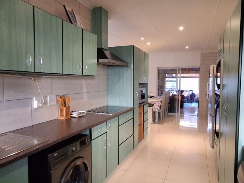 A functional kitchen featuring green cabinetry, a stainless steel sink, built-in oven and hob, tiled backsplash, and polished floor tiles.