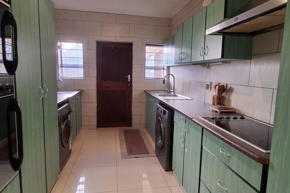 A functional galley-style kitchen featuring green cabinetry, integrated appliances, tiled backsplash, and ample counter space with a central access door.
