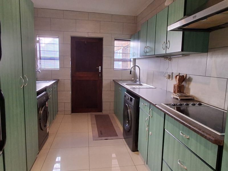 A functional galley-style kitchen featuring green cabinetry, integrated appliances, tiled backsplash, and ample counter space with a central access door.