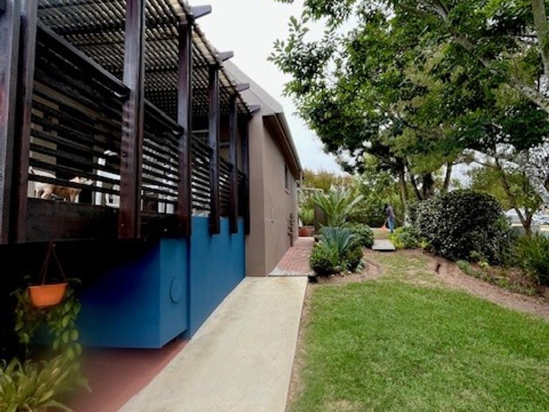A well-maintained rear exterior view featuring a timber pergola structure, a concrete pathway, and a landscaped garden area.