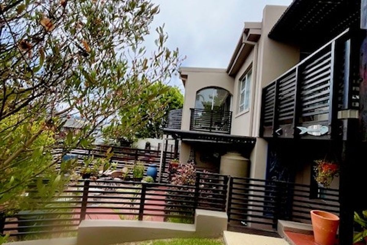 Rear view of the property featuring a landscaped garden, tiled patio area, and a balcony with slatted timber railings.
