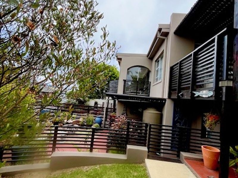 Rear view of the property featuring a landscaped garden, tiled patio area, and a balcony with slatted timber railings.