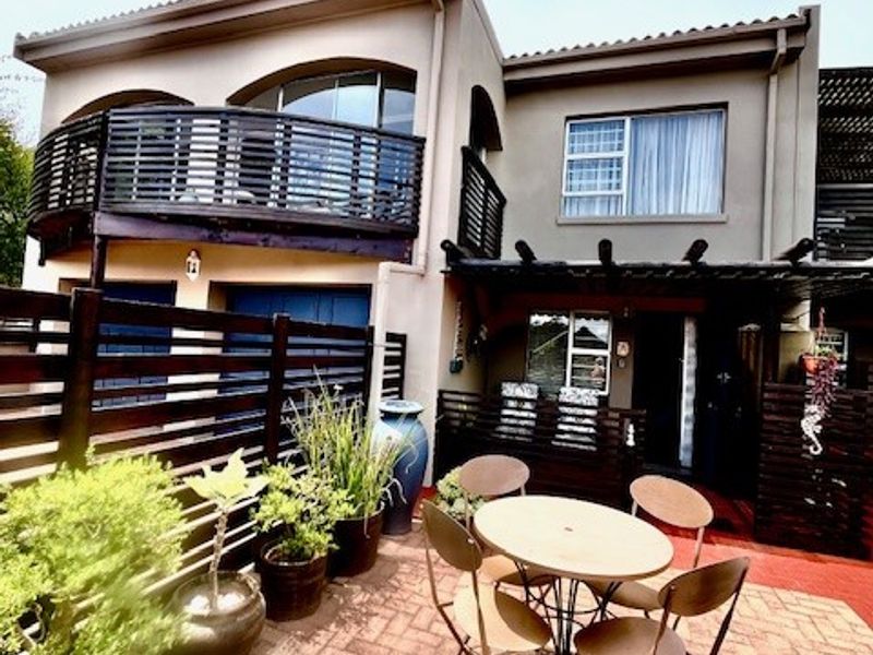 Rear exterior view featuring a paved patio area, a covered pergola, and an upper-level balcony with timber balustrading.