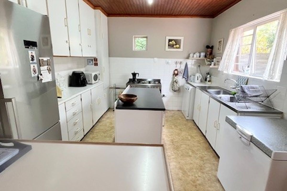 A functional kitchen featuring timber ceilings, ample built-in cabinetry, a central island, and a double sink with a tiled splashback.