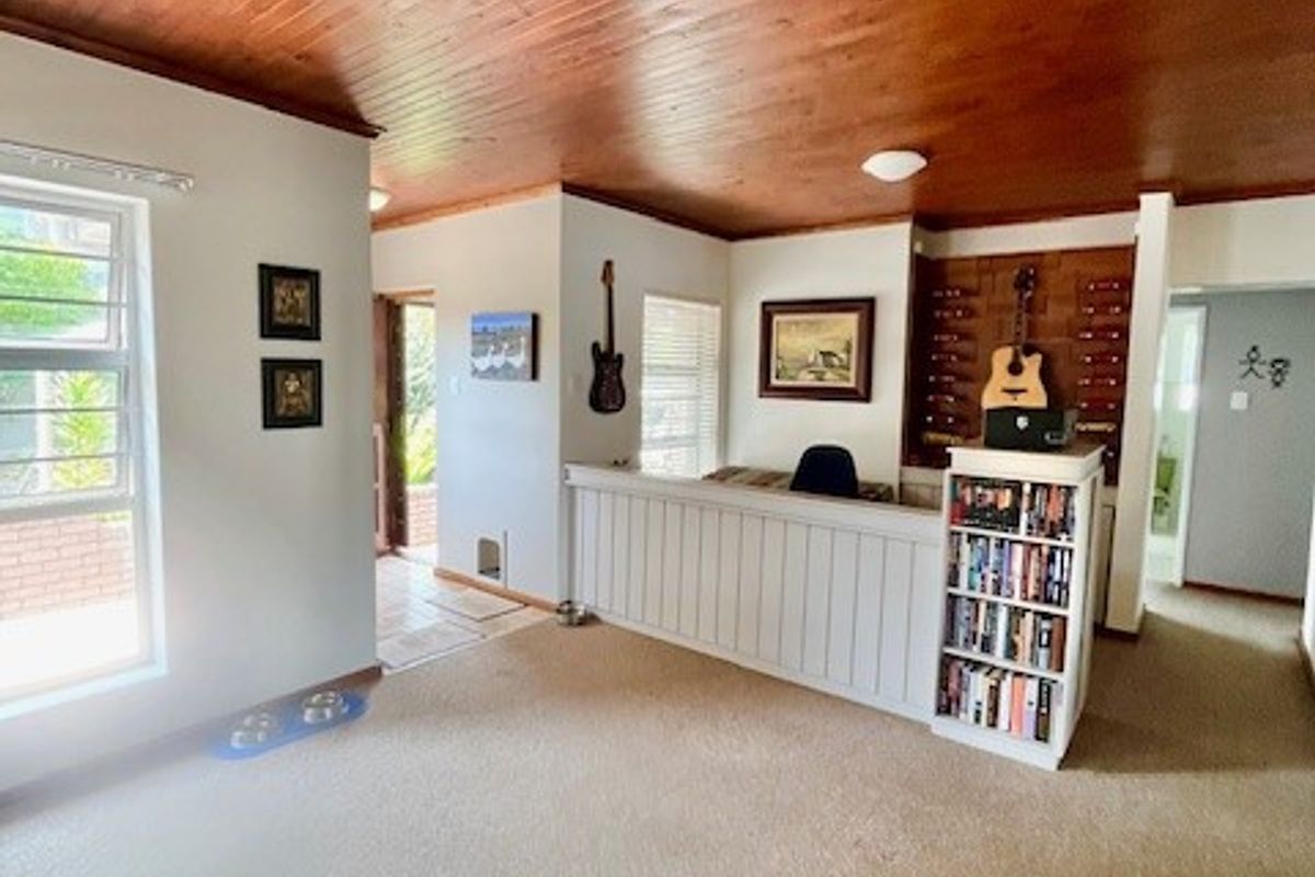A living area featuring a distinctive timber tongue and groove ceiling, carpeted flooring, and a built-in partition wall creating a semi-private space.