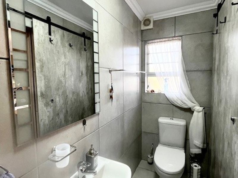 A compact, modern bathroom featuring a vanity basin, toilet, and large wall-mounted mirror with neutral grey tiled finishes.