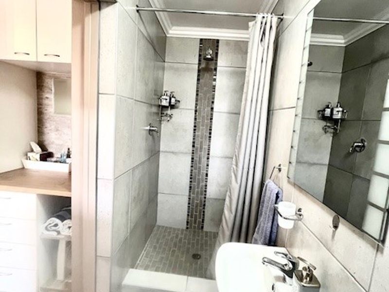 A functional bathroom featuring a walk-in shower with tiled accents, a pedestal basin, and a large wall-mounted mirror.