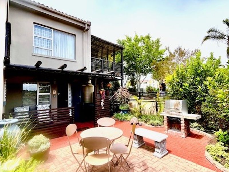 A well-maintained outdoor patio area featuring brick paving, a built-in brick braai, and a timber pergola, providing a functional space for outdoor entertaining.