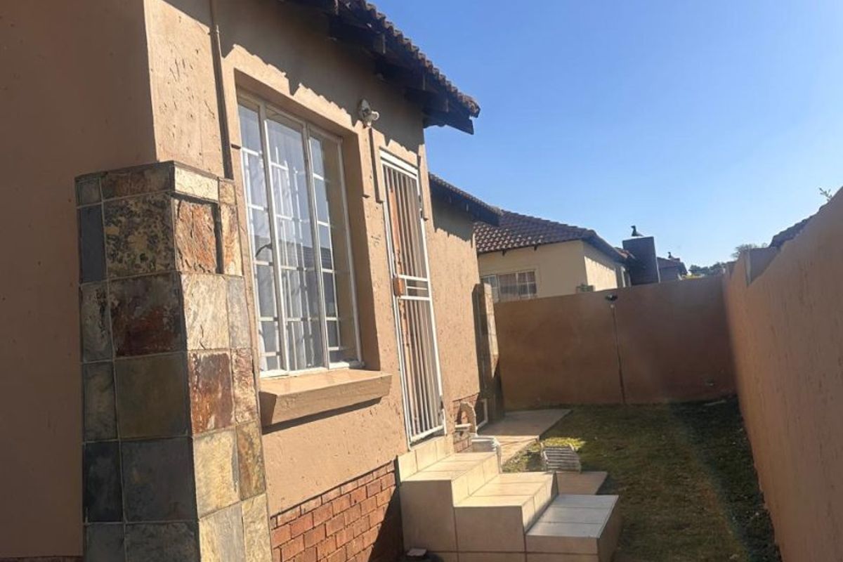 Rear exterior view of the house featuring a stone-clad pillar, brick base, tiled steps, and a private garden area enclosed by a perimeter wall.