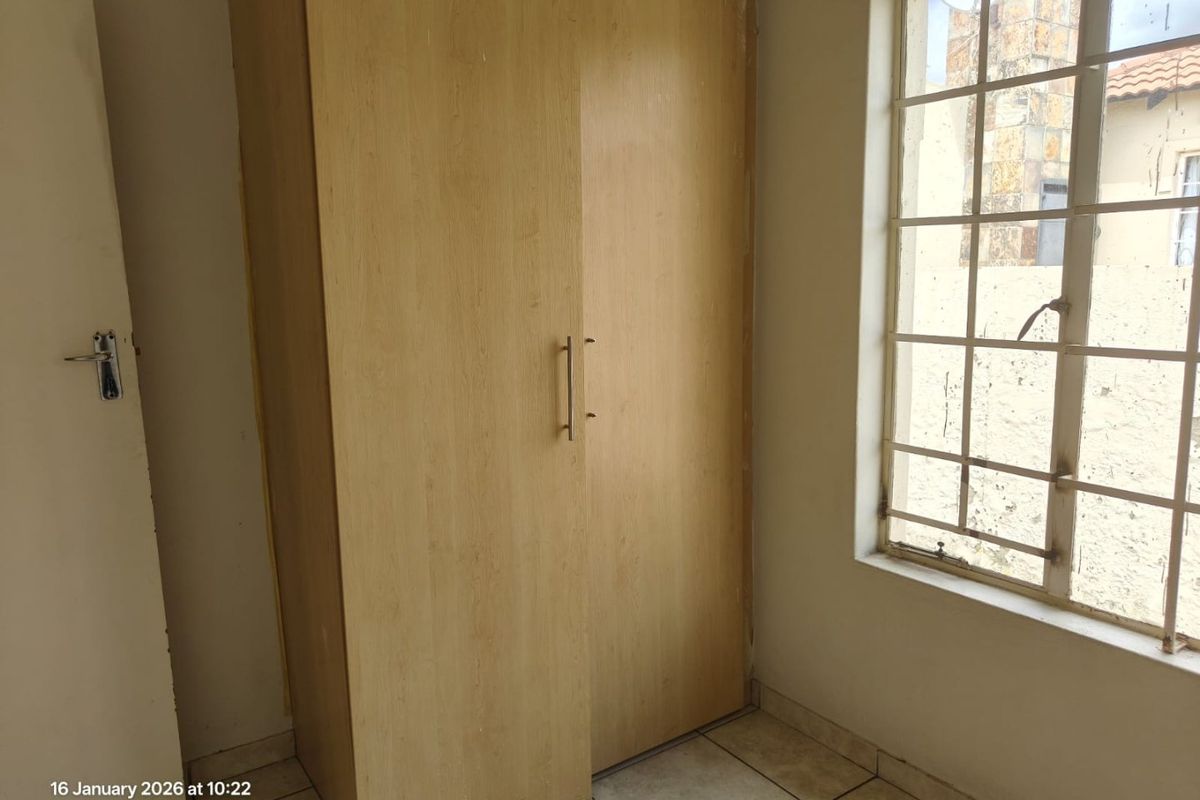 A bedroom featuring built-in light wood cabinetry and a window with security bars, finished with tiled flooring.